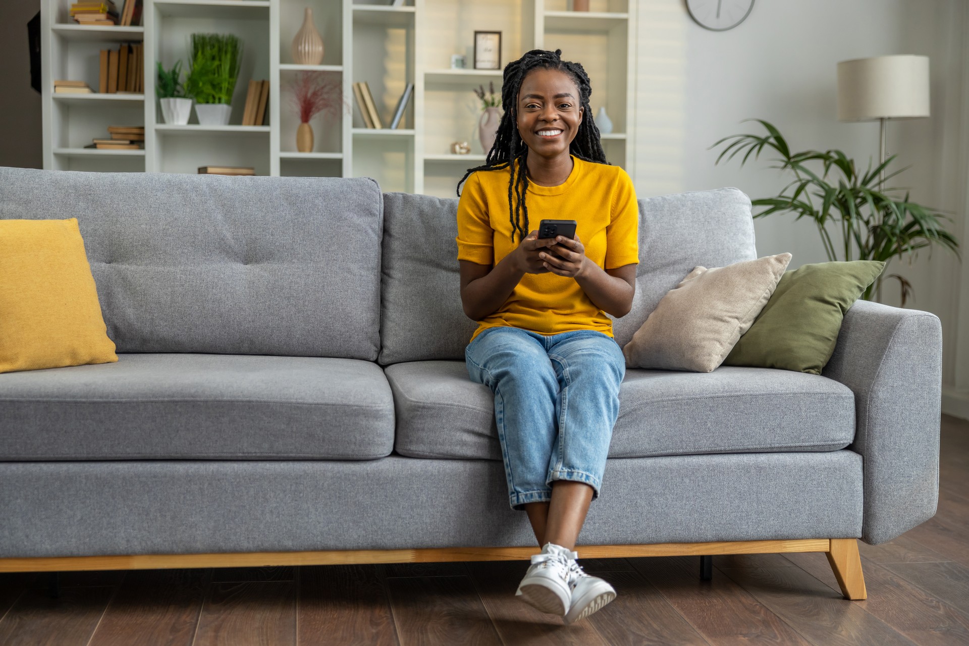 Smiling dark-skinned girl sitting on a sofa with a phone in hands